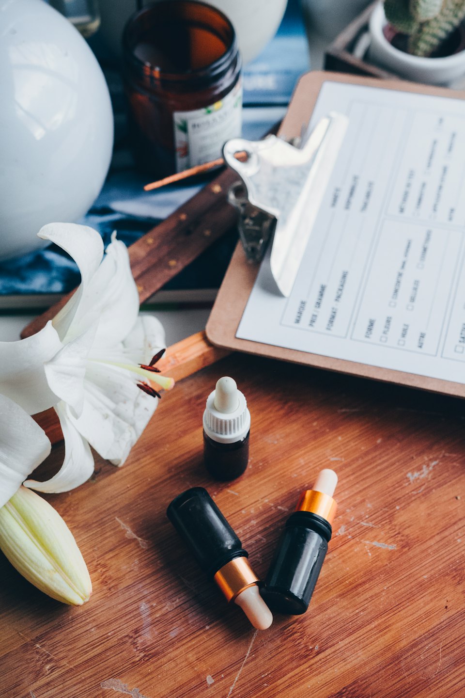 Skincare dropper bottles and lily on a wooden table.