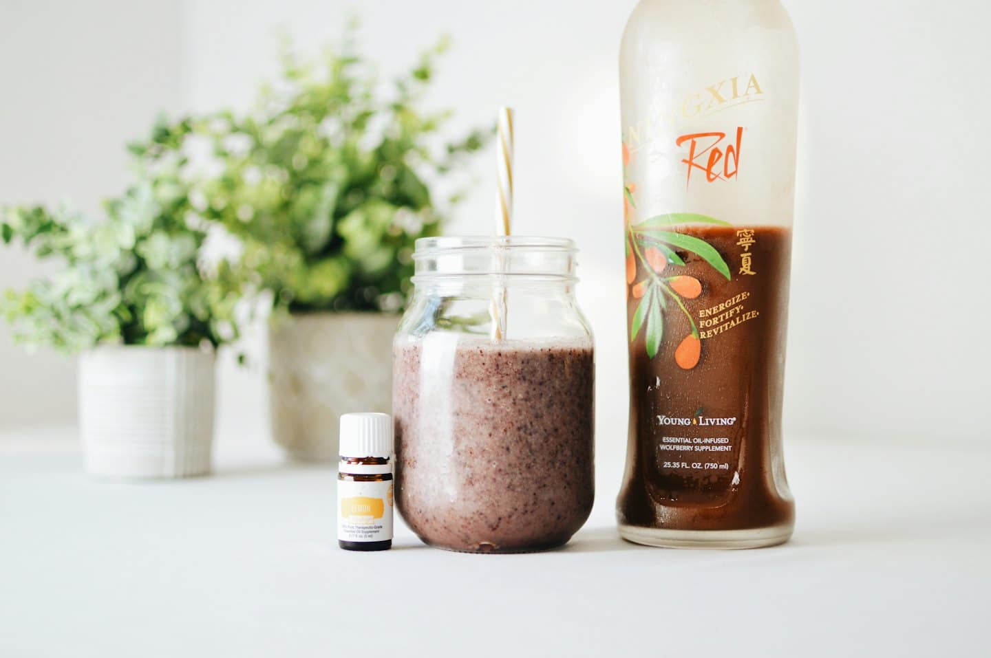 Purple smoothie, essential oil, and red liquid bottles on white surface.