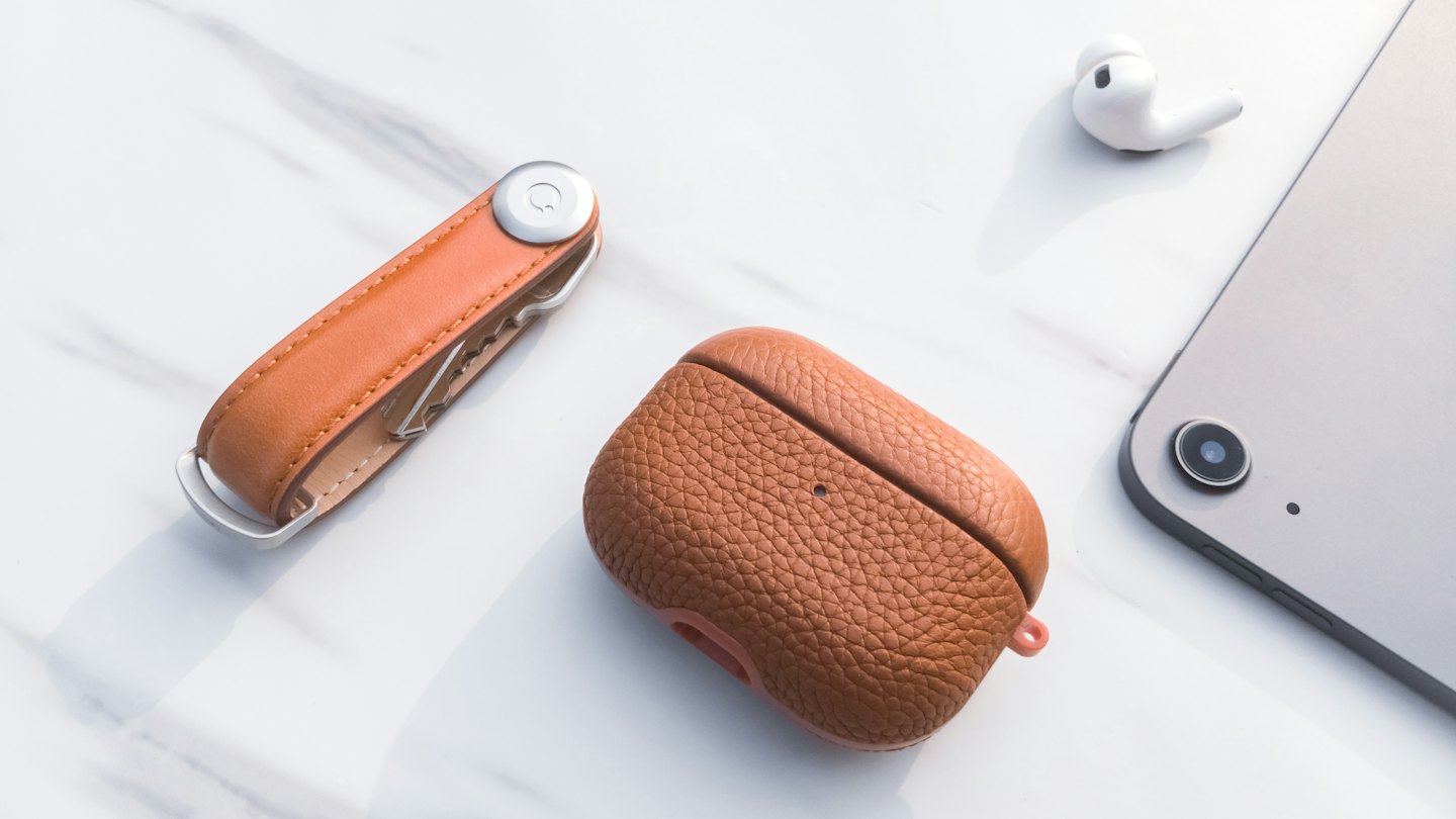 Tan leather key organizer and brown earbud case on marble.